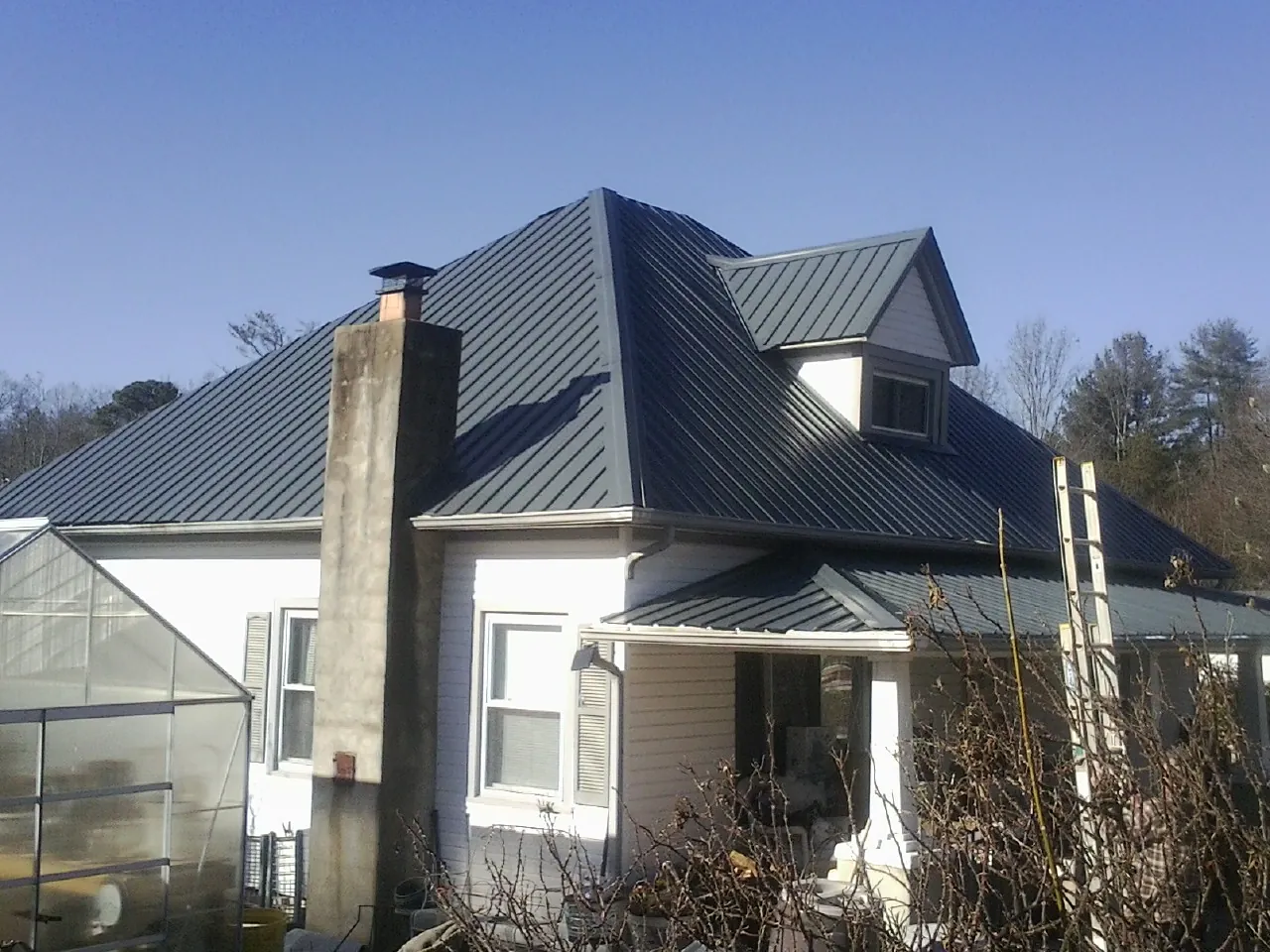 Dark blue standing seam metal roof on a white farmhouse with dormer — Slate & Tile Roof Repair by Roofing Brothers in Shickley