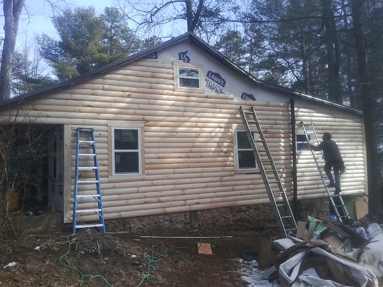 Ladders set against fresh log siding during an exterior remodel in Shickley