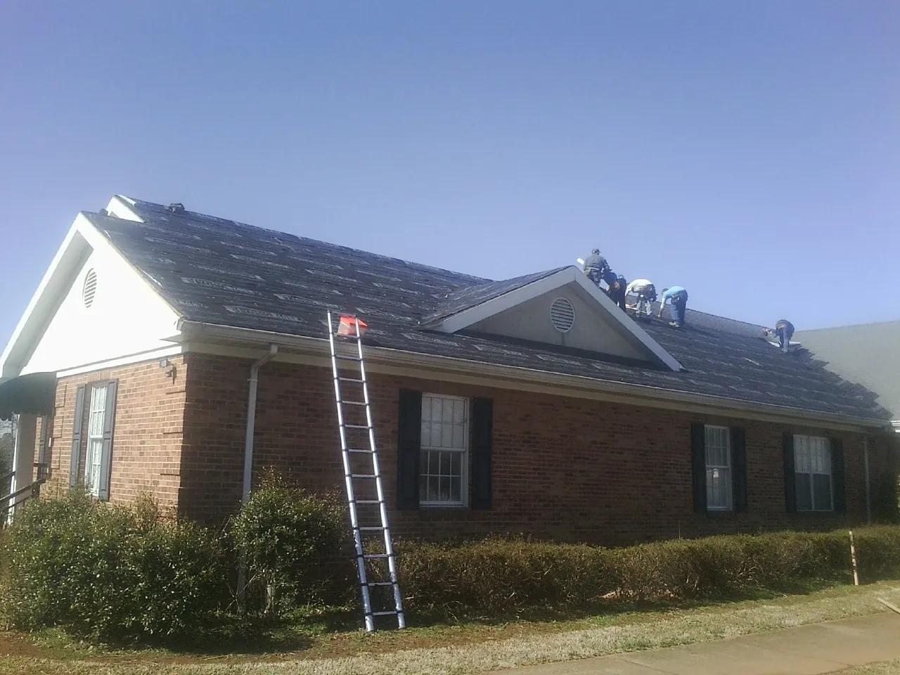Crew tearing shingles off a brick ranch roof with a ladder set — Emergency Roof Repair work by our crew in Shickley