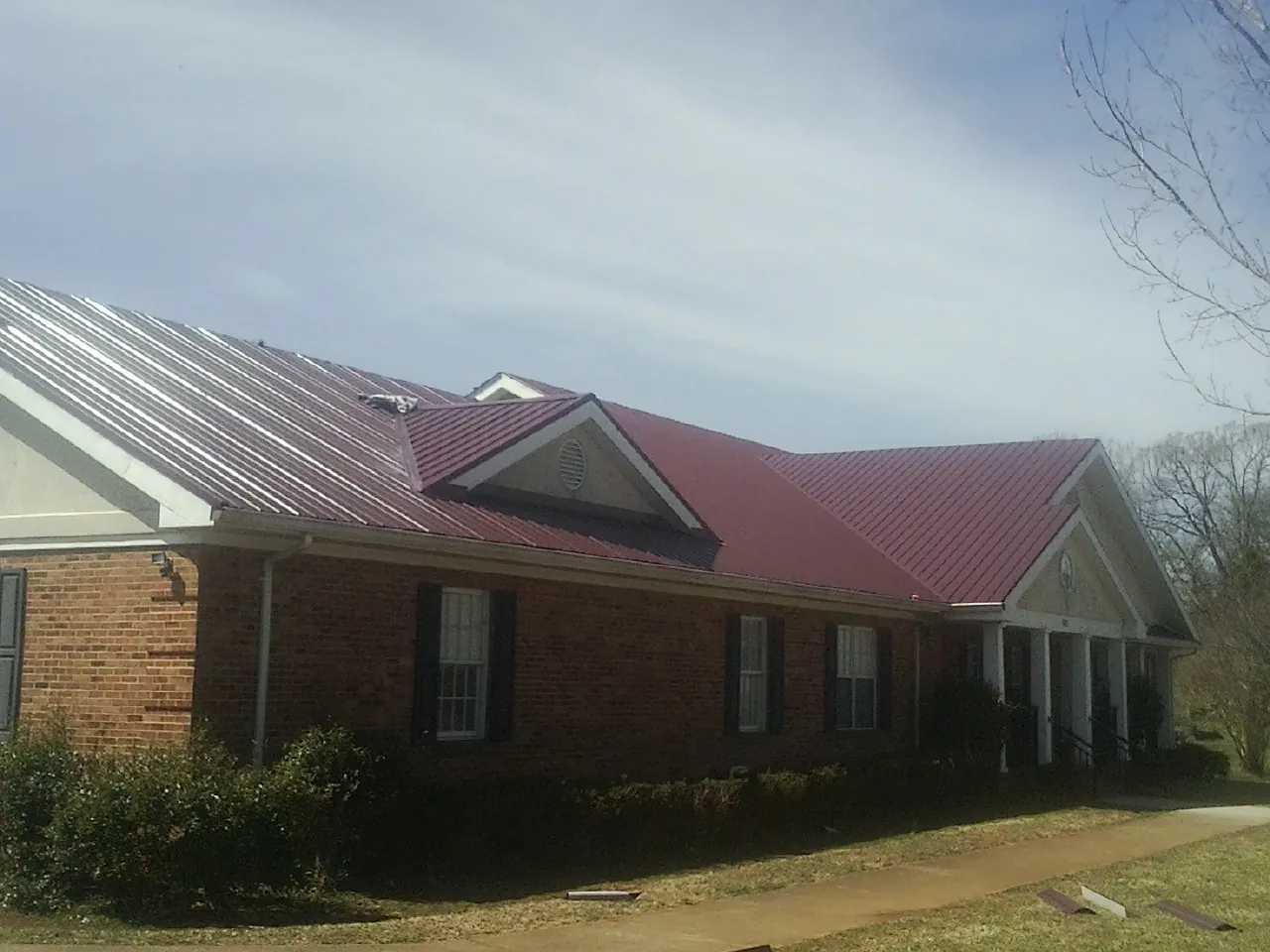 Red metal roof with gabled entries on a long brick building, from a Hail Damage Roof Repair job in Shickley