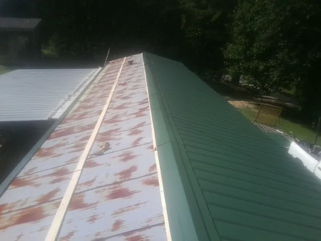 Old rusted panels beside newly installed green metal roofing — Wind Damage Roof Repair by Roofing Brothers in Shickley