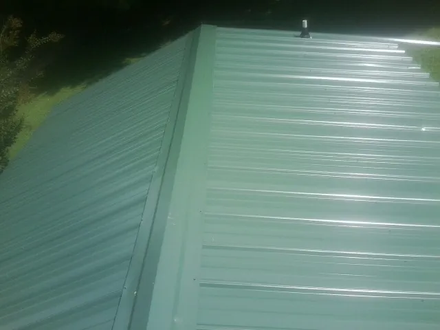 New green metal panels meeting at the ridge of a roof — Flat Roof Repair work by our crew in Shickley