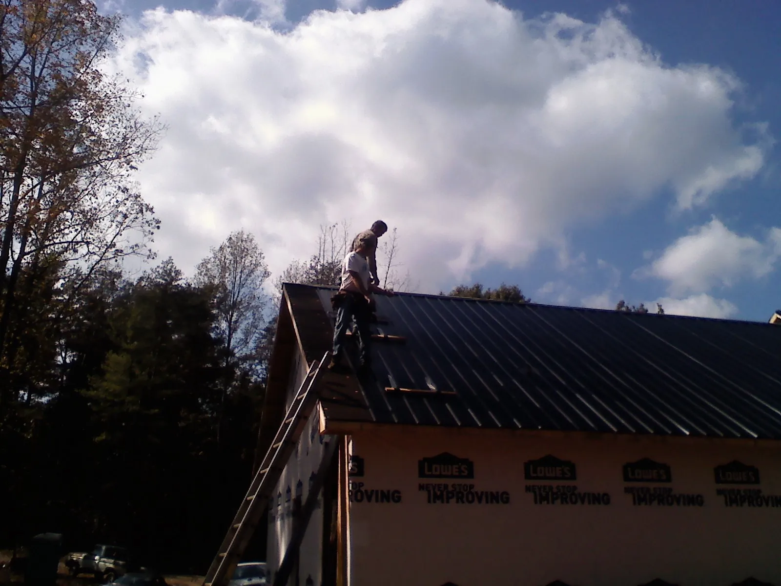 Roofer fastening dark metal panels high against a cloudy sky, from a Roof Inspection job in Shickley