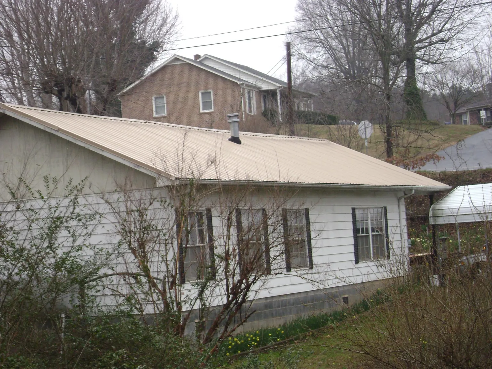 Tan metal roof on a white sided house set into a hillside — Commercial Roofing by Roofing Brothers in Shickley