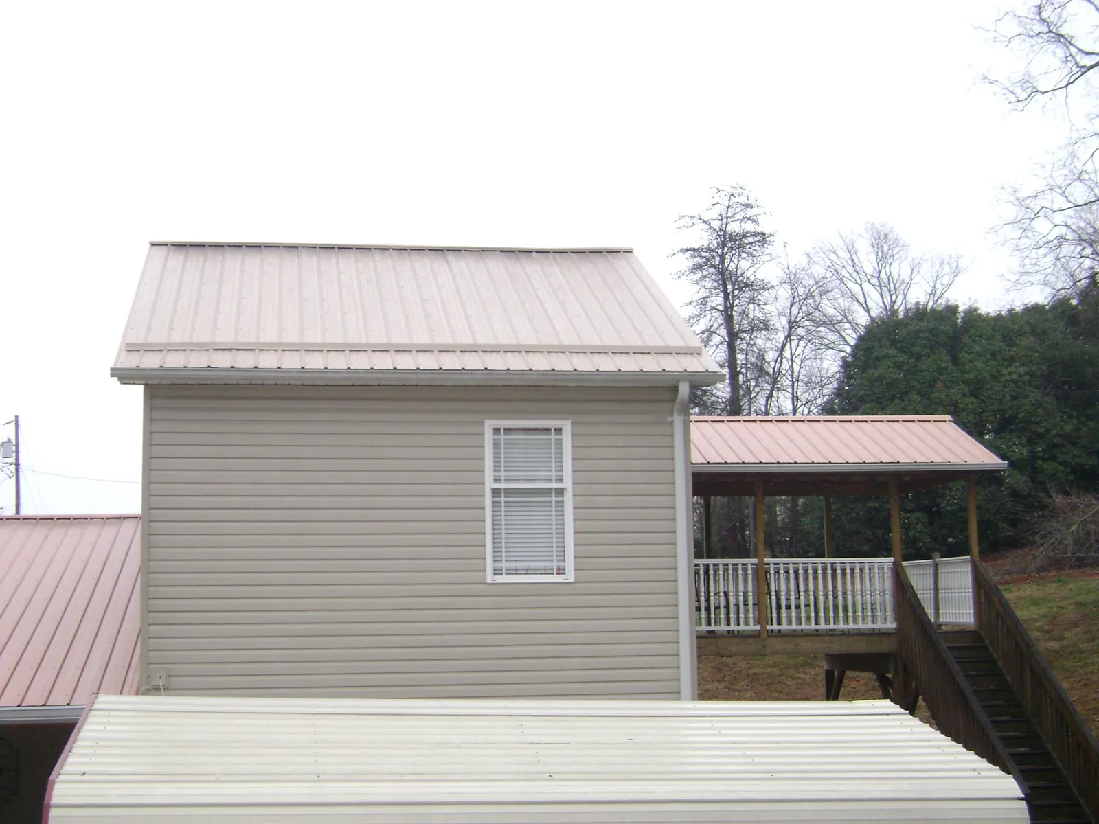Tan metal roofs on a two story addition and attached porch, from a Roof Replacement job in Shickley